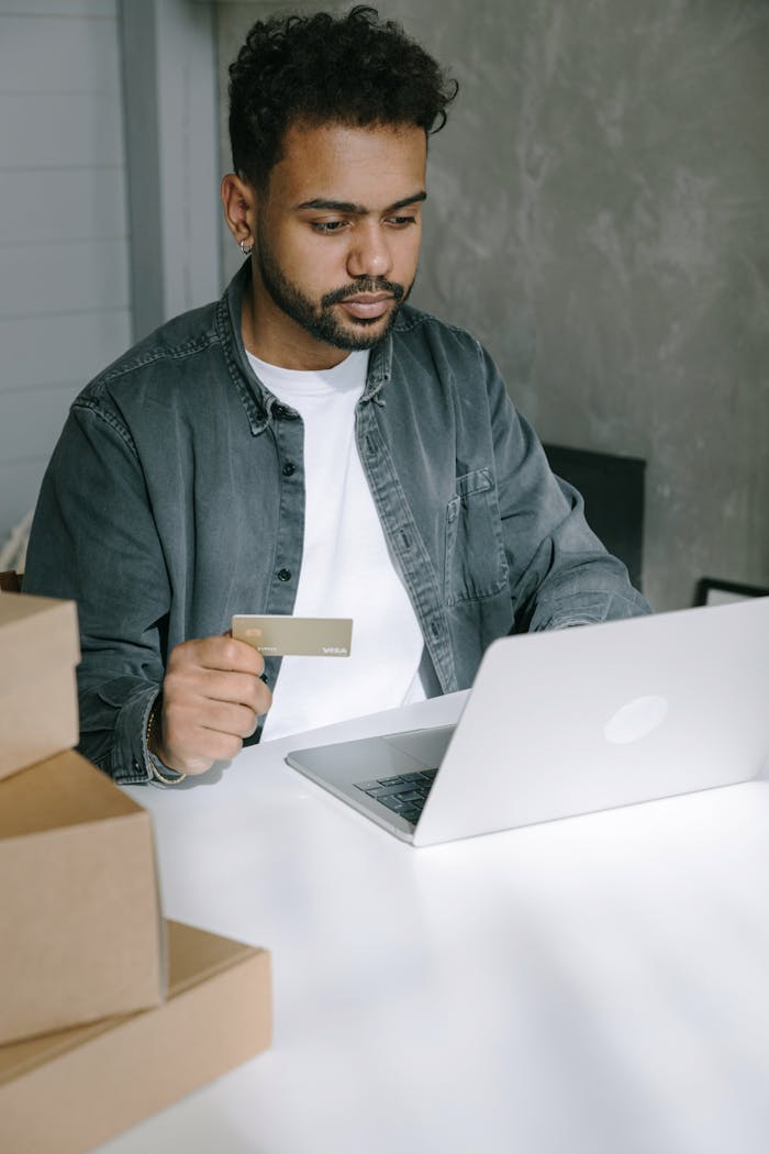 Young man using laptop and card for online shopping at home.